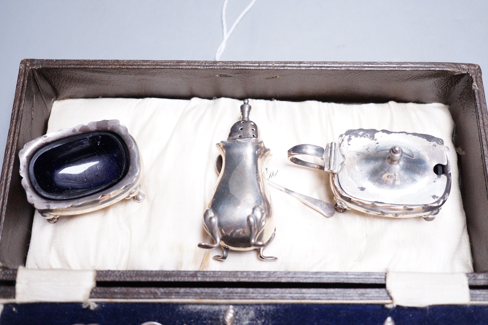 A cased George V silver three piece condiment set, two other silver condiments and a plated condiment.